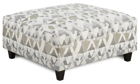 A large square cocktail ottoman in fabric upholstery of modern triangle shapes in shades of gray white tan and charcoal.