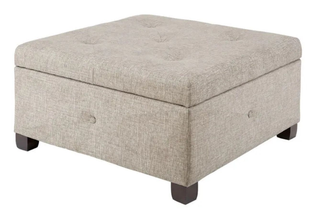 A square-shaped, beige button-tufted storage ottoman with dark brown wooden legs.